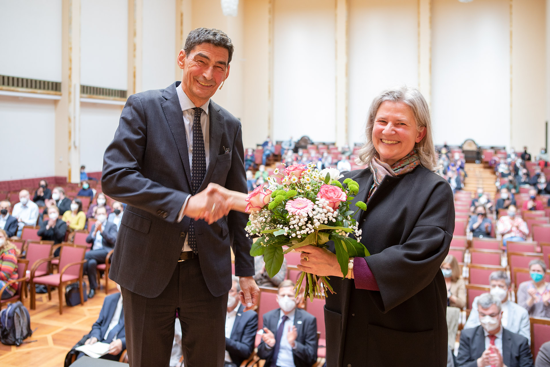 Bernhard Sibold shakes Karla Pollmann's hand, she holds a bouquet of flowers in her other hand.