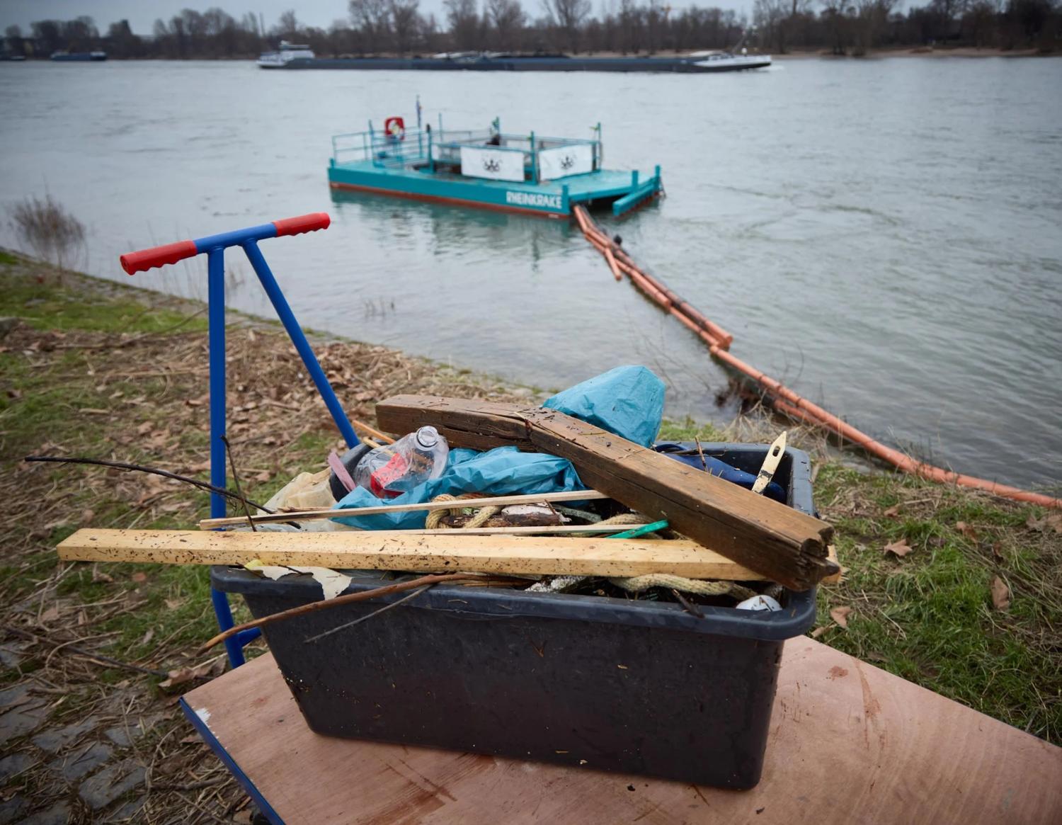 Kiste mit Müll, im Hintergrund der Rhein mit der schwimmenden Müllfalle