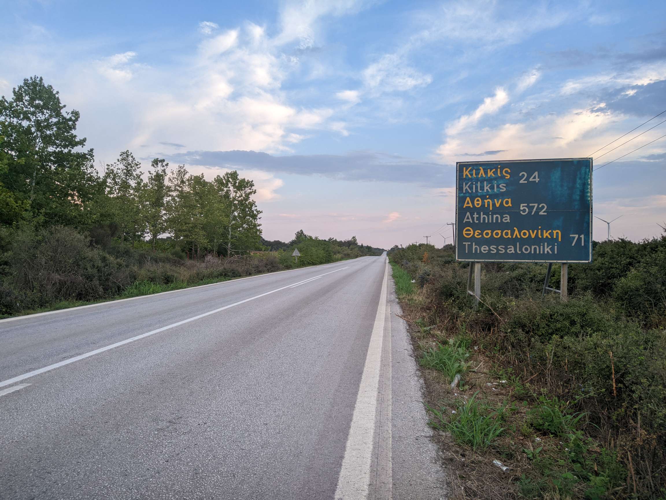 Straße in Griechenland und Schild mit griechischen und lateinischen Buchstaben und Kilometerangaben