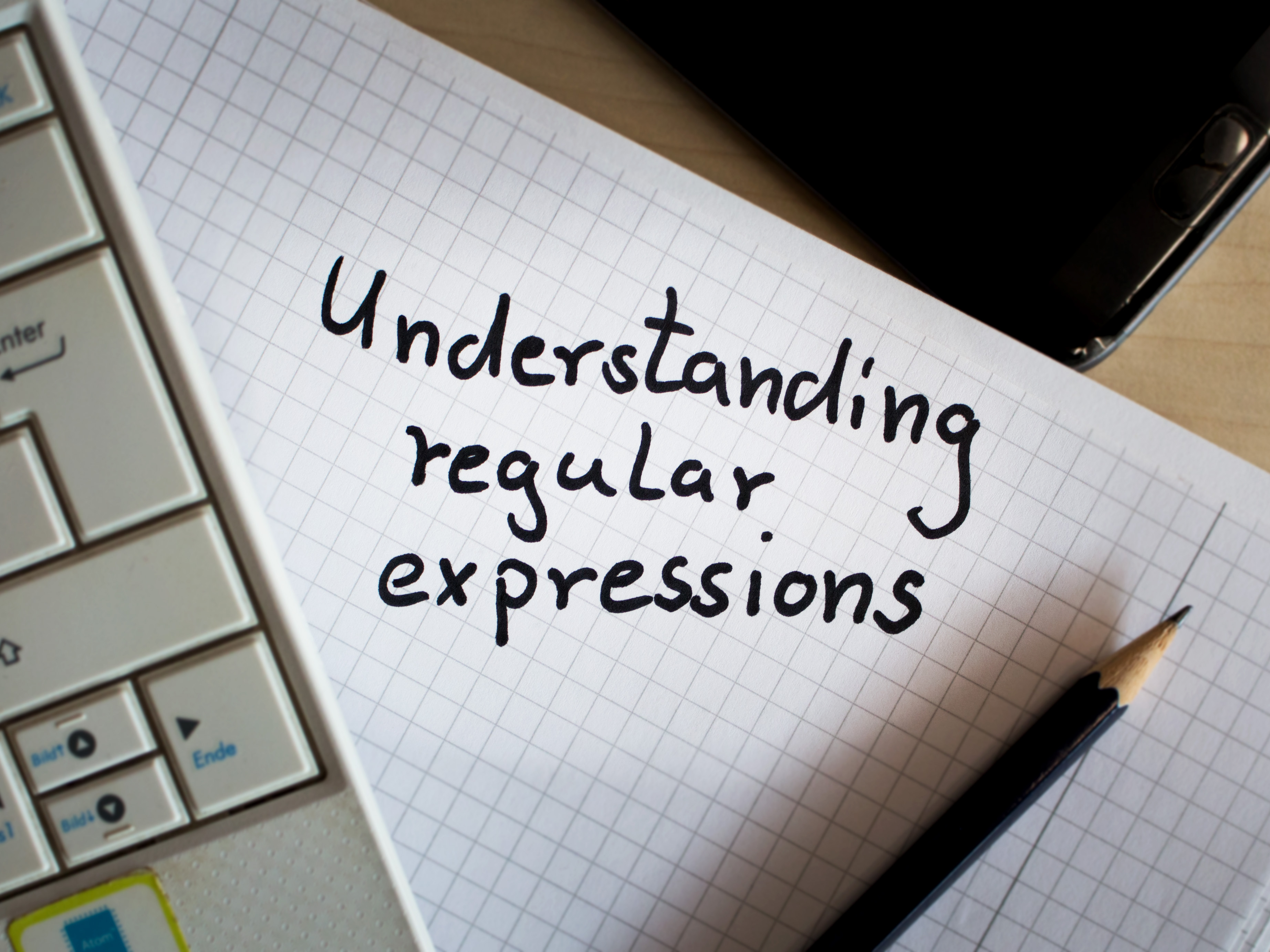 [Translate to Englisch:] Understanding regular expressions written on note next to keyboard and pencil