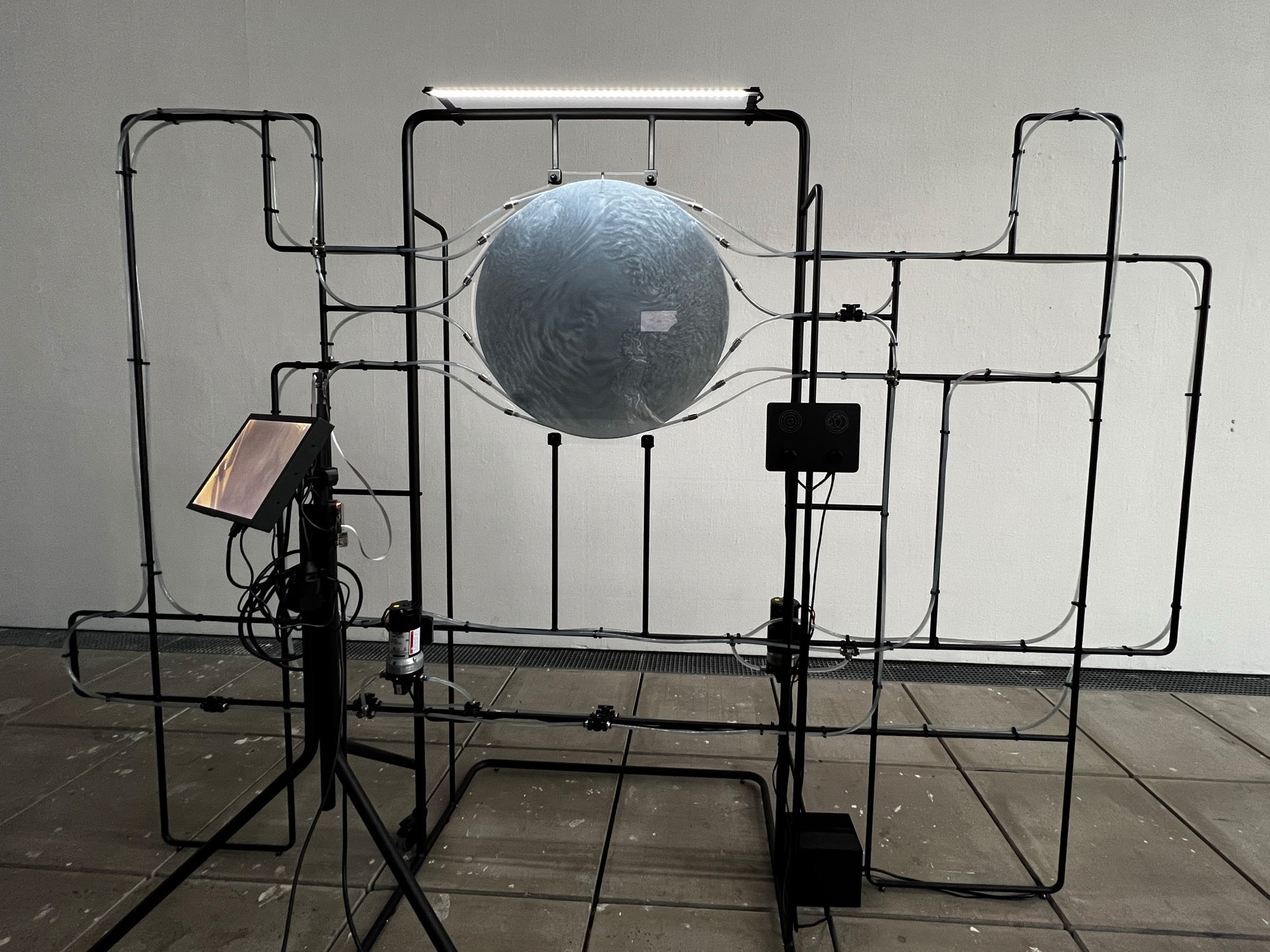 Photo of a disc suspended from a black wire frame with several hoses coming off it (=water circuit). 