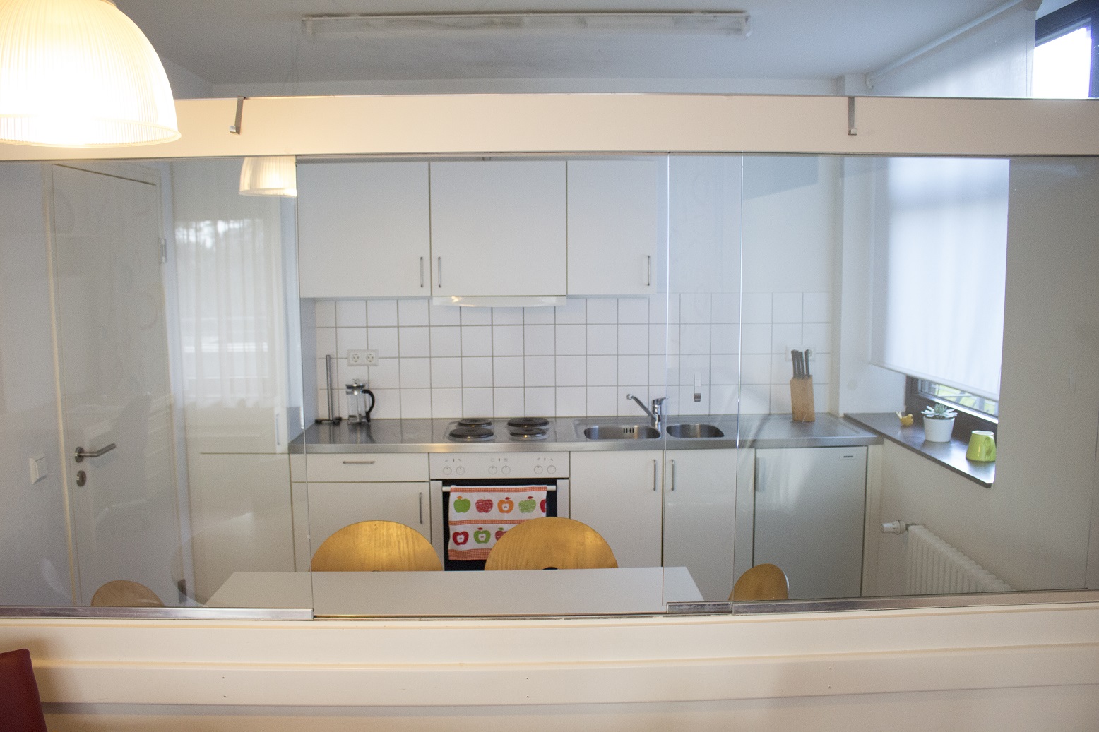 Küchenzeile im Hintergrund mit Kühlschrank, 4 Herdplatten und Waschbecken, im Zentrum befindet sich ein Esstisch für 4 - 6 Personen