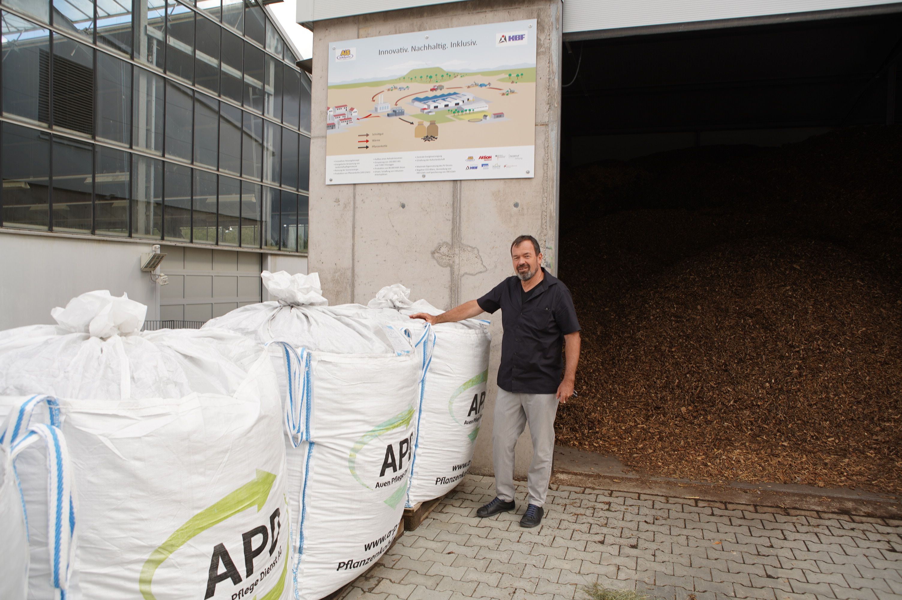 The picture shows Marcus Hölz, managing director of AiS inklusiv gGmbH, standing next to sacks filled with biochar.