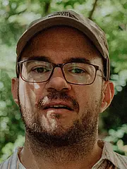 Porträtfoto von Daniel Maier mit Blättern im Hintergrund.