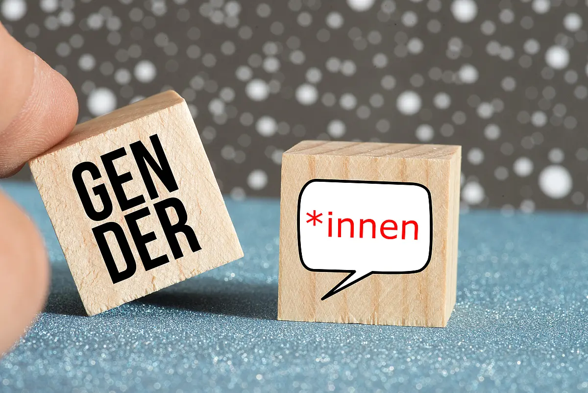Bild auf dem Finger mit zwei Holzwürfeln mit der Aufschrift Gender und „*innen spielen