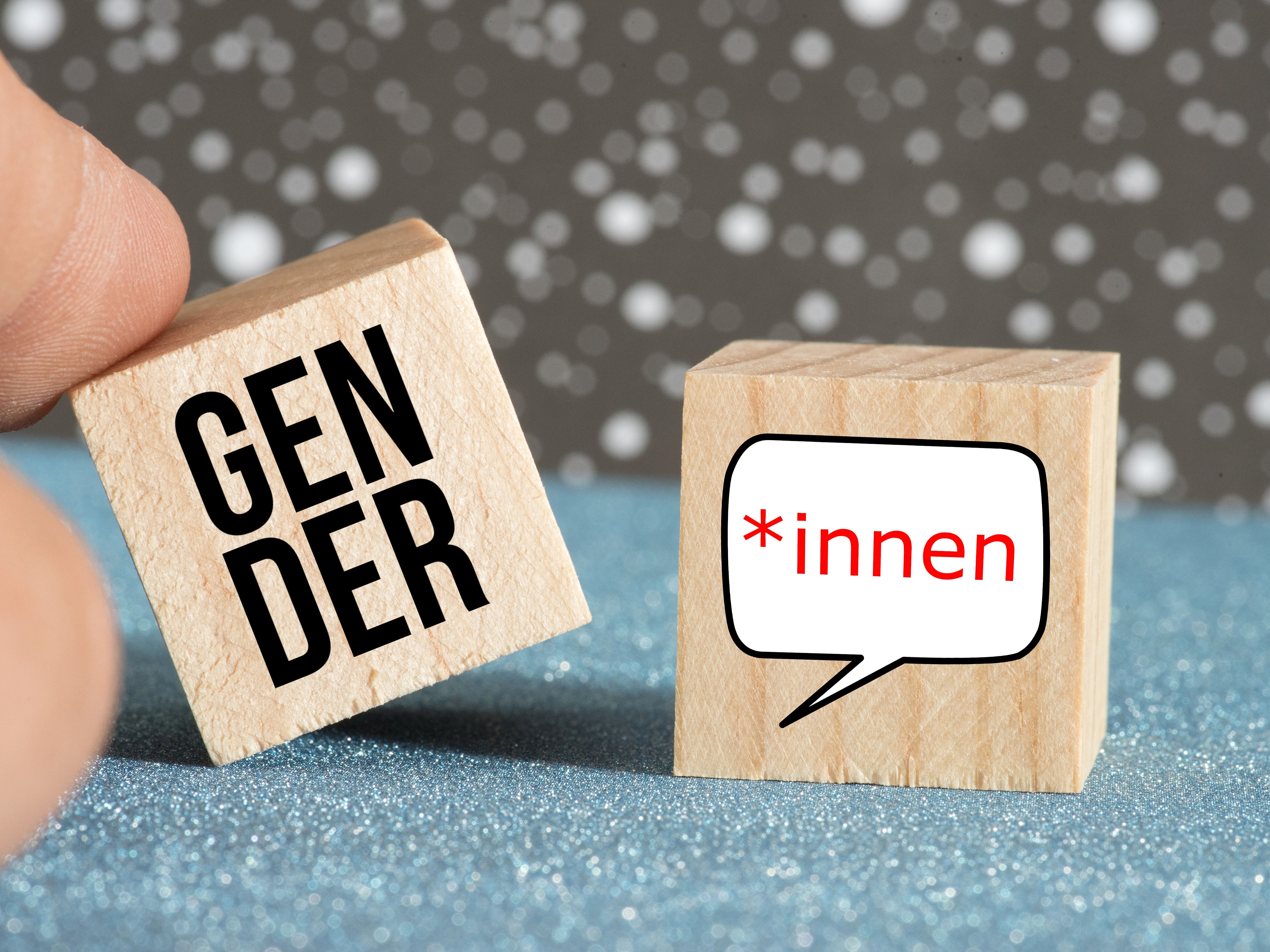 Kachelbild auf dem Finger mit zwei Holzwürfeln mit der Aufschrift Gender und „*innen spielen (Link zur Seite Gendersensible Sprache)