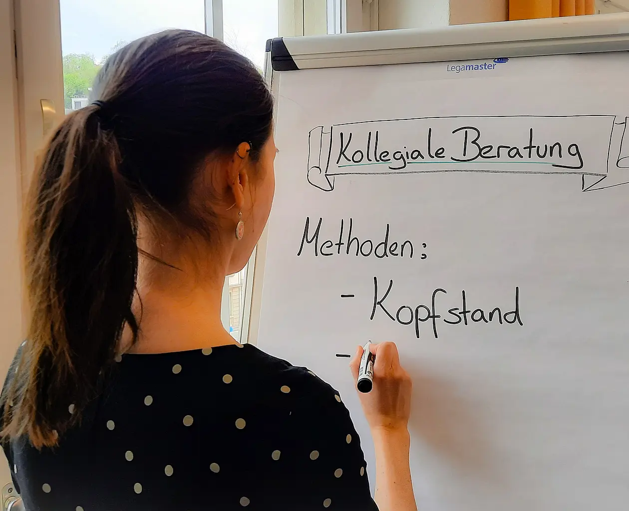 Eine Frau schreibt auf eine Flipchart. Auf der Flipchart steht Kollegiale Beratung, Methoden: Kopfstand.