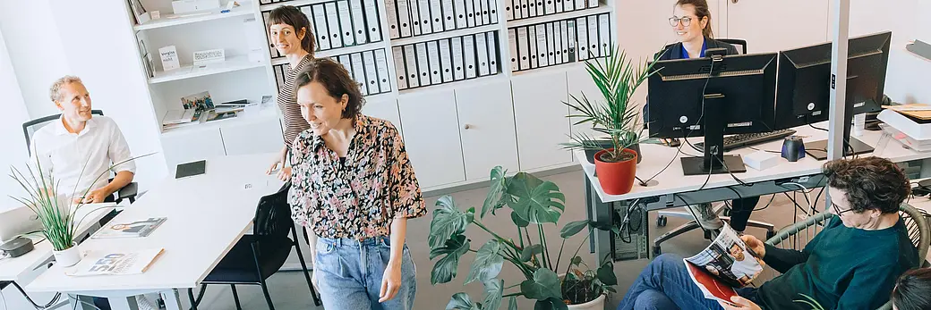 Menschen in einem Büro, zwei Personen stehen, drei Personen sitzen