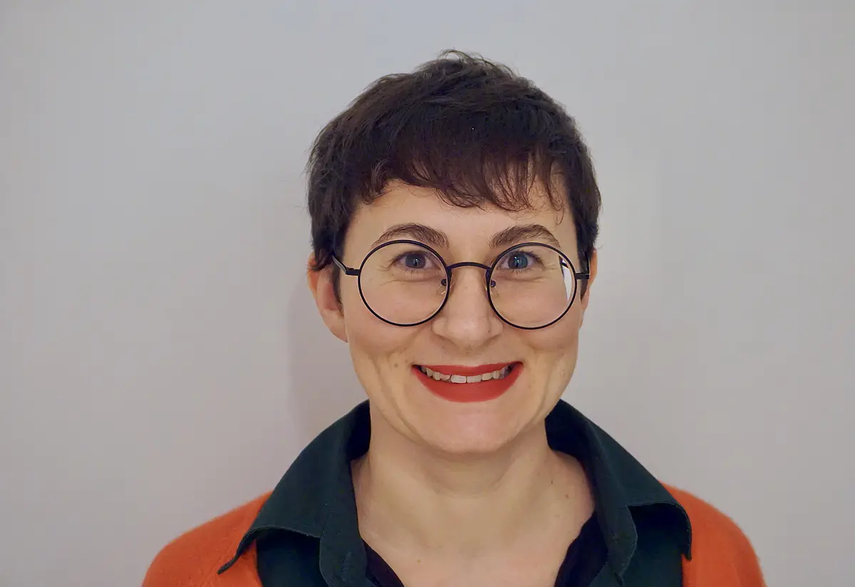 Frau um die 40 mit kurzen, dunklen Haaren und großer, runder Brille