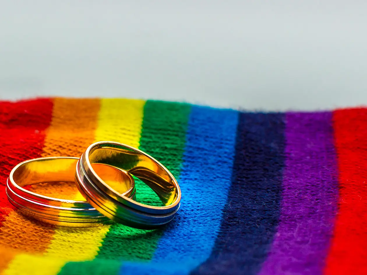 Eheringe liegen auf Stoff in Regenbogenfarben