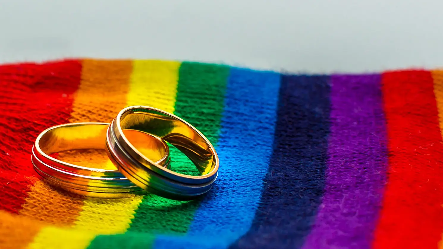 Eheringe liegen auf Stoff in Regenbogenfarben