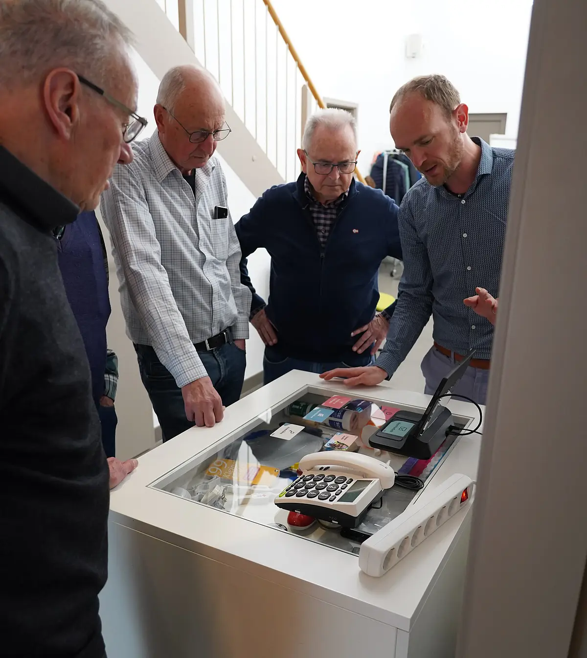 Four men are standing around a table on which there are telephones and other objects.
