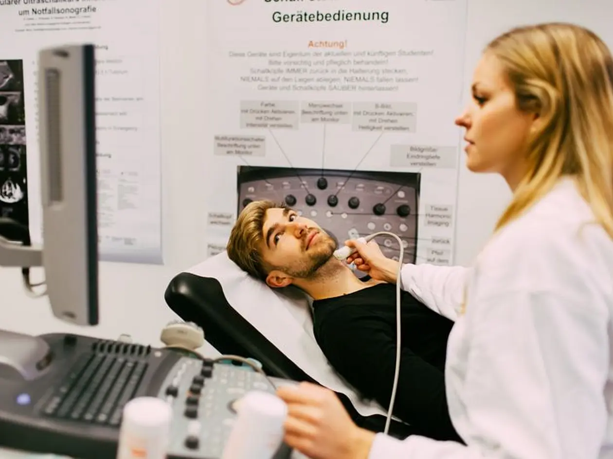 Eine Medizinstudentin untersucht einen jungen Mann mit einem Ultraschallgerät am Hals