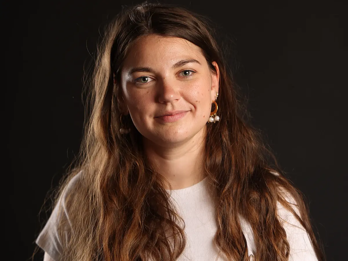 Das Foto zeigt Armelle Ballian in die Kamera lächelnd im Portrait vor einem schwarzen Hintergrund.