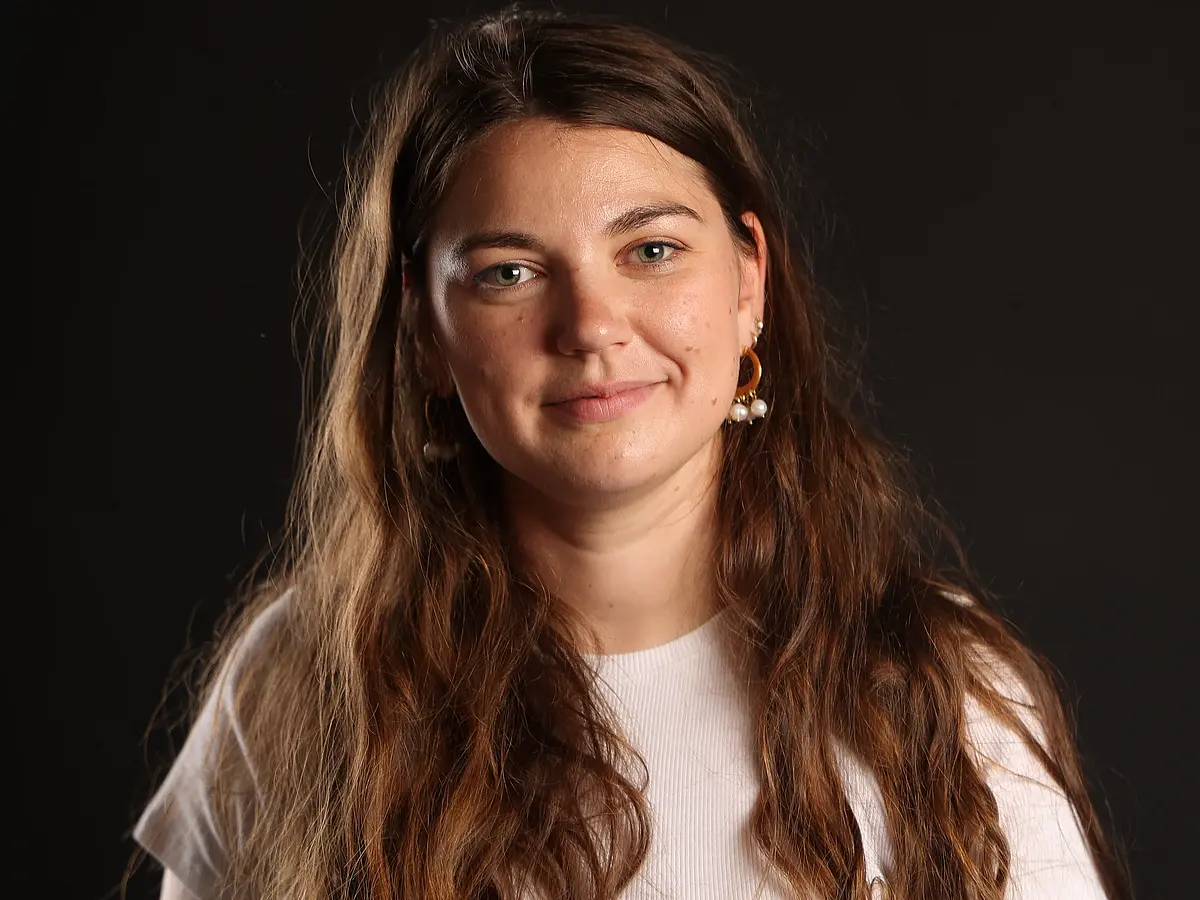 Das Foto zeigt Armelle Ballian in die Kamera lächelnd im Portrait vor einem schwarzen Hintergrund.