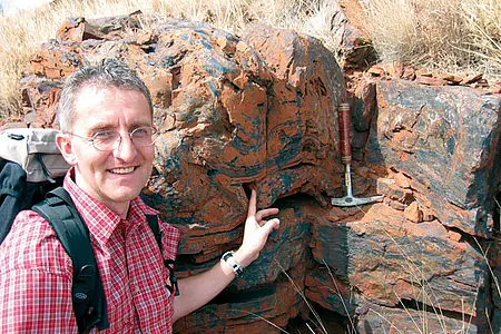Andreas Kappler zeigt alternierende Schichten von schwarzen und orangefarbenen Eisen- und Silikatmineralen in 2,5 bis 2,6 Milliarden Jahre alten präkambrischen gebänderten Eisenformationen (Gamohaan Hill, in der Nähe von Kuruman, Northern Cape Province
