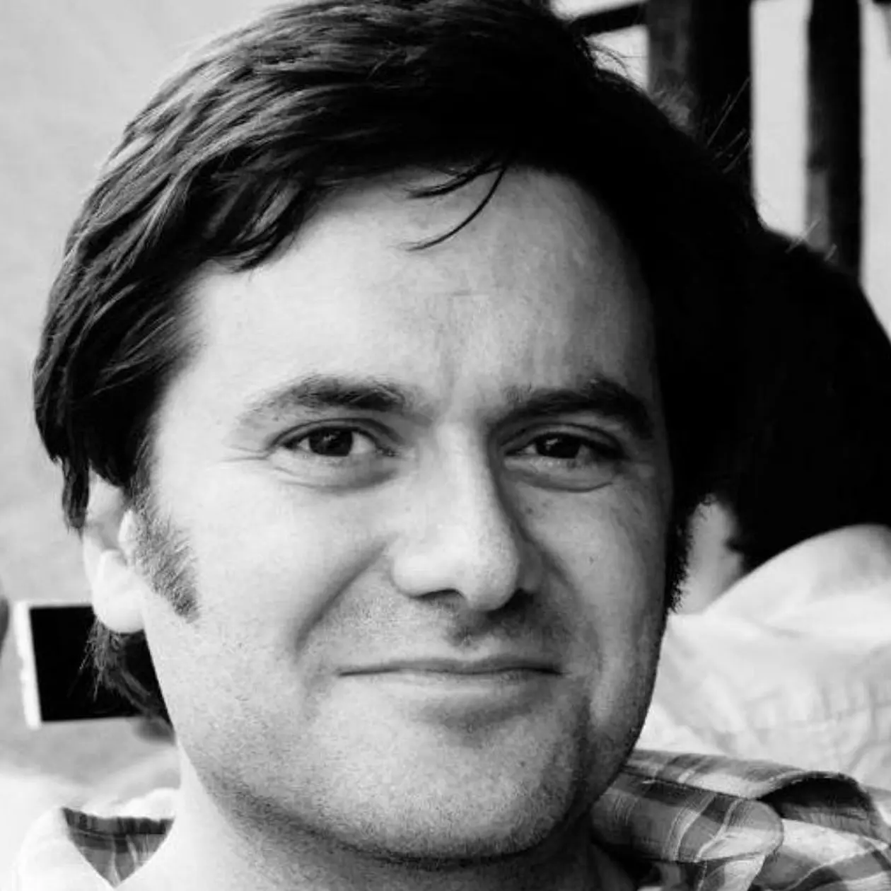 Black and white portrait of Claudio Tennie, a white man with short dark hair, facing the camera smiling. 