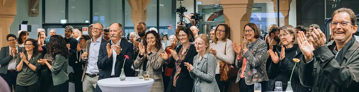 Viele Personen klatschen bei einer Veranstaltung in die Hände und sind sehr erfreut.