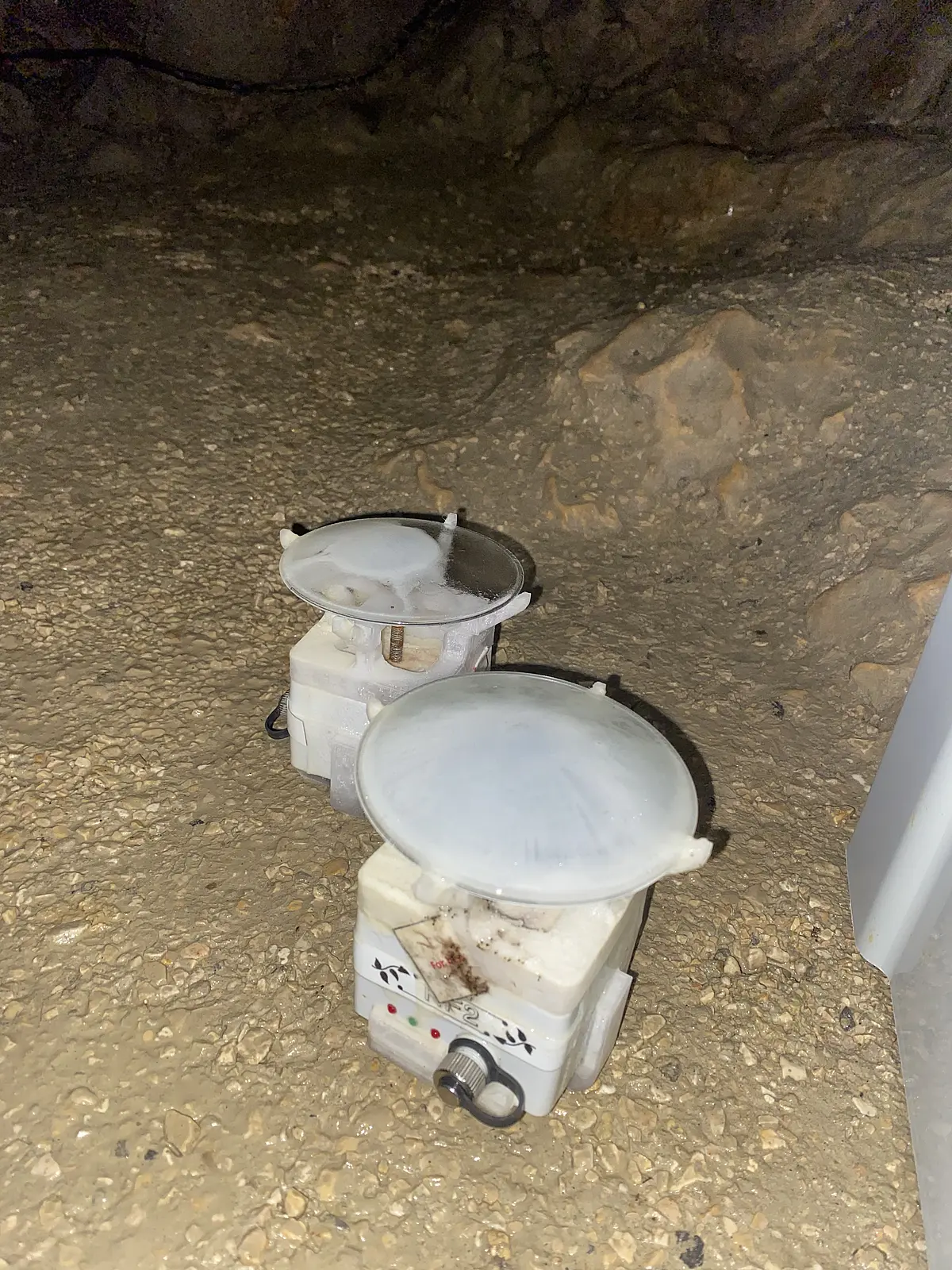 Zwei Tropfwasserlogger stehen hintereinander auf Höhlenboden. Auf den Uhrengläsern sind weiße Kalzitausfällungen zu sehen.