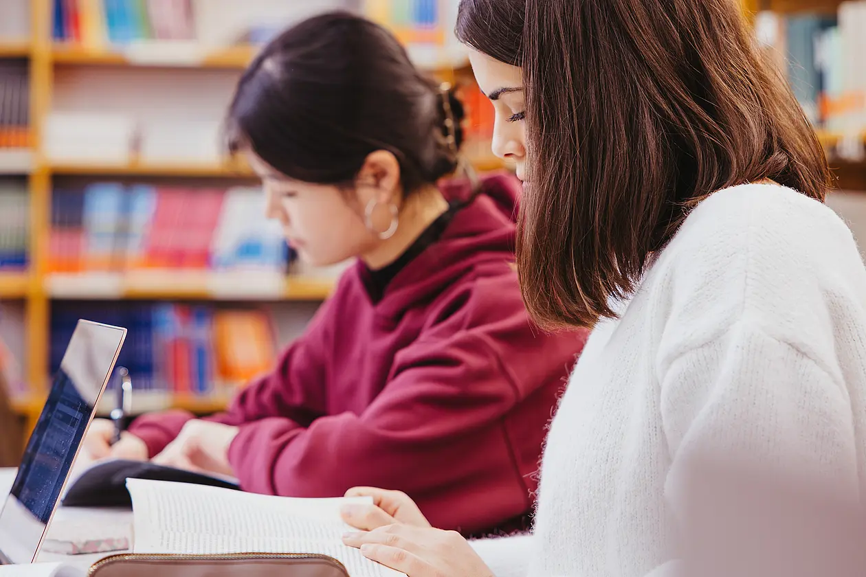 Zwei Studentinnen sitzen lesend in der Bibliothek.