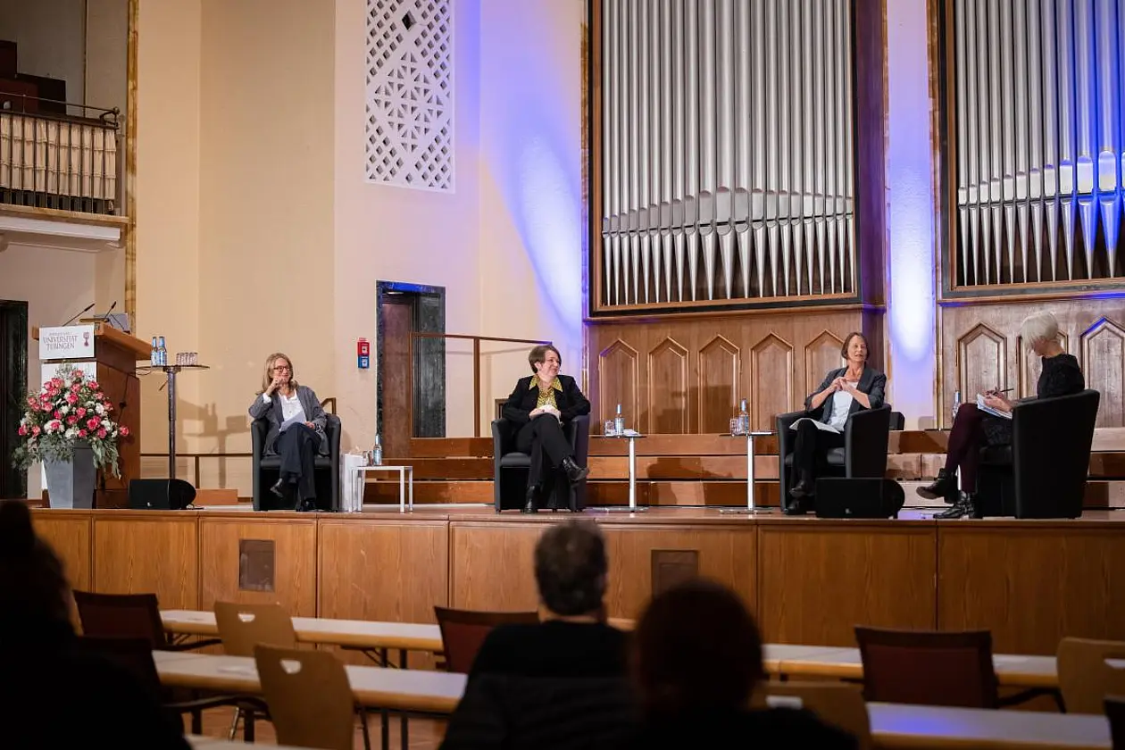 Four female scientists sit on the stage of the University of Tübingen's ballroom. A large organ can be seen in the background.
