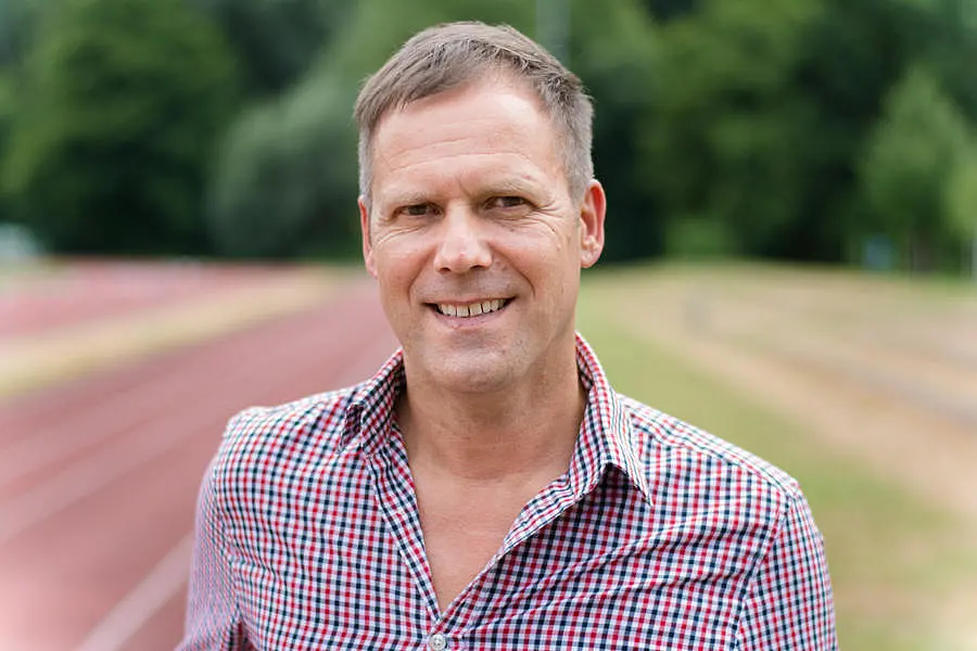 Porträtfoto von Professor Dr. Ansgar Thiel, im Hintergrund ist ein Sportplatz zu sehen.