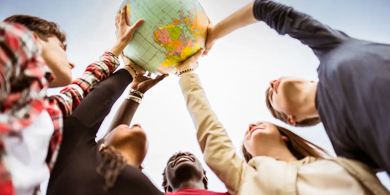 Five persons hold a globe and look up into the sky.