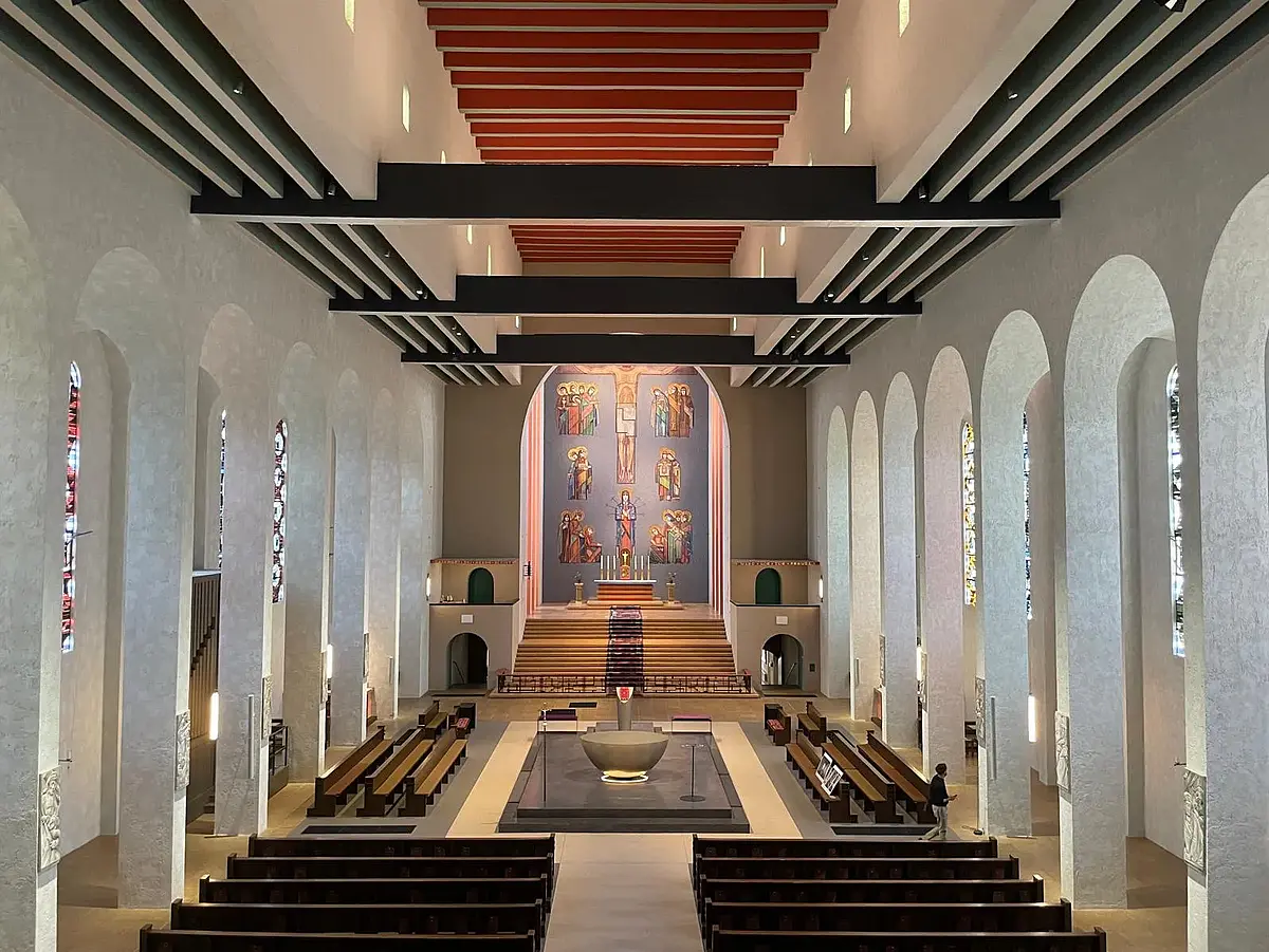 Auf diesem Bild blickt man von der Empore auf ins Kircheninnere hinunter. Die hintere Wand der Kirche wird von einem die ganze Wand umfassenden Bild eingenommen. Das Bild zeigt den gekreuzigten auf blauem Hintergrund. Unter ihm sind insgesamt 19 Personen mit heiligen Schein (+ Maria) in kleinen Grüppchen von zwei bis vier Personen zu sehen. Die Kirche verfügt darüber hinaus über einen sog. Hochaltar, der an der hinteren Wand steht. Er erhebt sich über das restliche Kirchenschiff, da er durch zwei Treppenabsätze und eine Absperrung vom restlichen Kirchenschiff getrennt ist. 