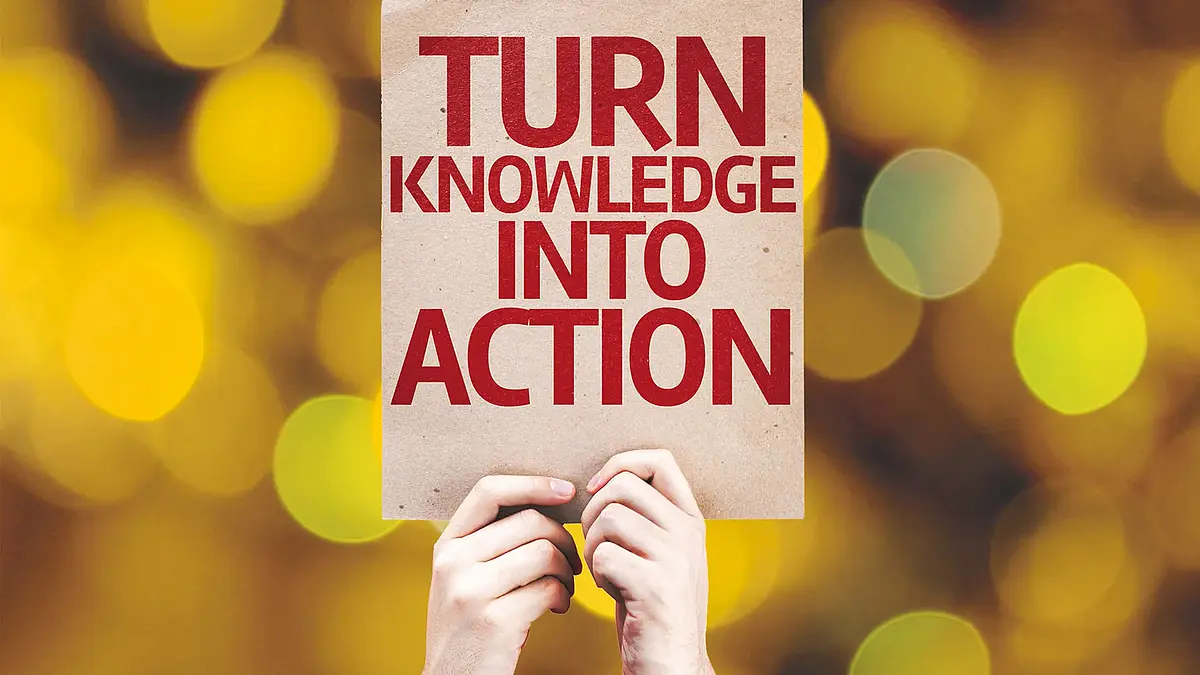 Zwei Hände vor Herbstblättern im Hintergrund recken ein Papierschild mit der Aufschrift Turn Knowledge into Action in die Höhe. Service-Learning