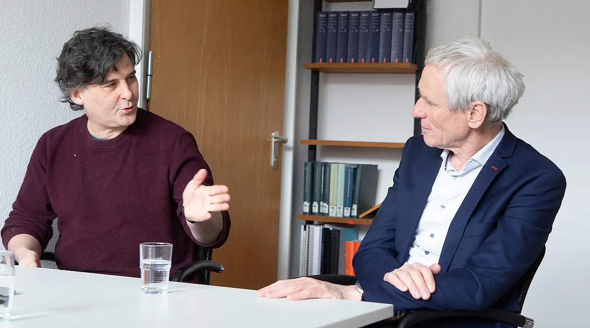 Der Historiker Ewald Frie und der Soziologe Boris Nieswand sietzen an einem Tisch und sind im Gespräch.