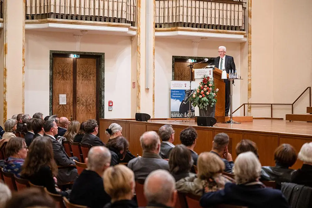 Winfried Kretschmann auf der Bühne am Rednerpult. Im Vordergrund das Publikum.