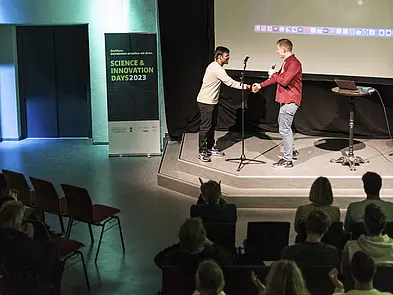 Zwei Personen geben sich auf der Bühne die Hand