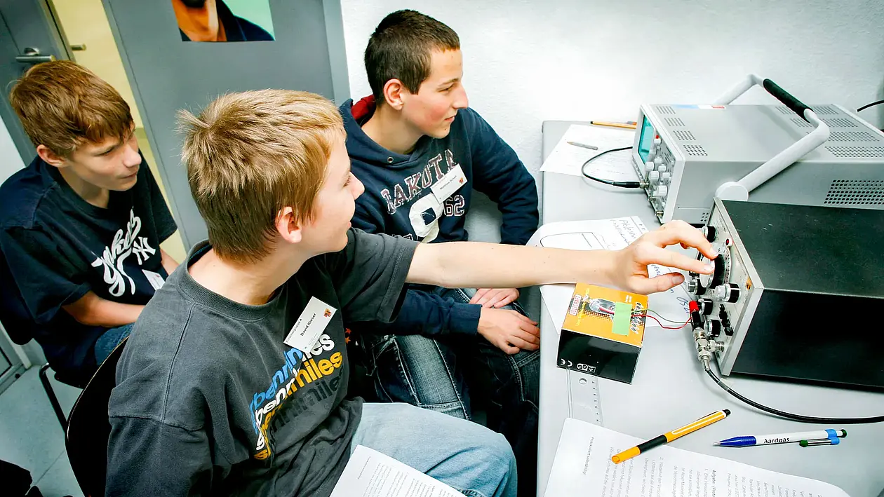 Drei Schüler sitzen in einem kleinen Raum und drehen an den Knöpfen eines Apparats.