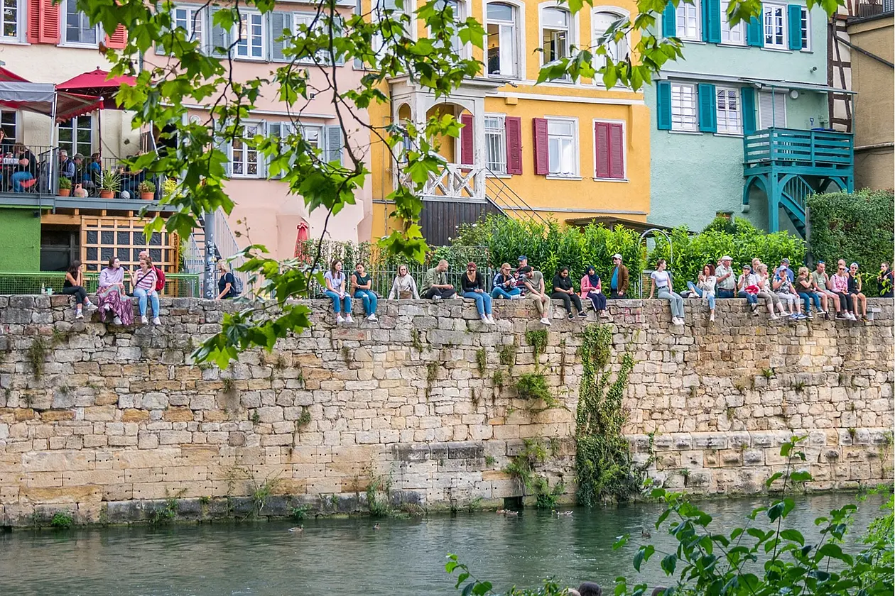 The Zwingelmauer in Tübingen, fully lined with people sitting and enjoying the view over the Neckar on a sunny day.