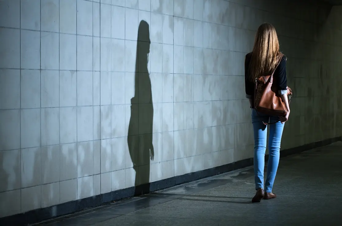 Frau in dunkler Bahnhofsunterführung, ihr Schatten wird an die Wand geworfen