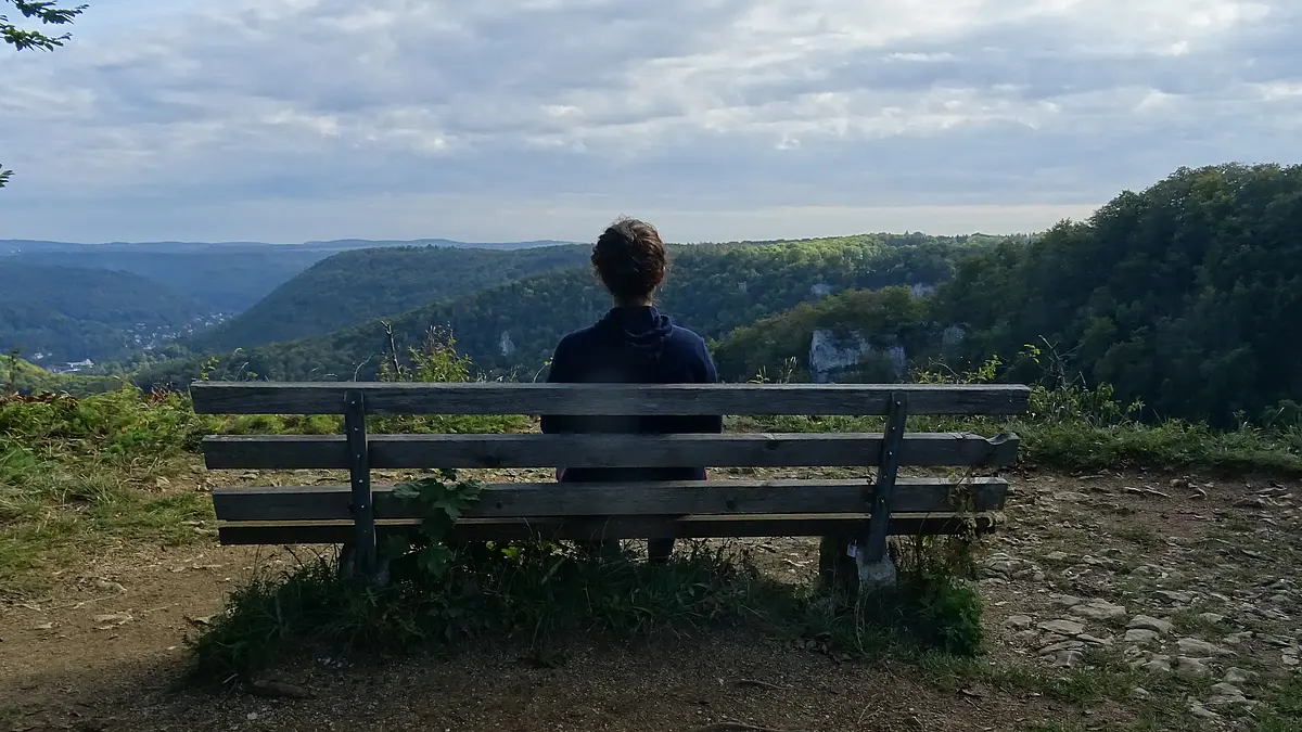 A young woman sits on a bench and looks into the wide horizon
