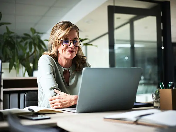Frau sitzt an einem Schreibtisch und schaut auf ein Laptop. 