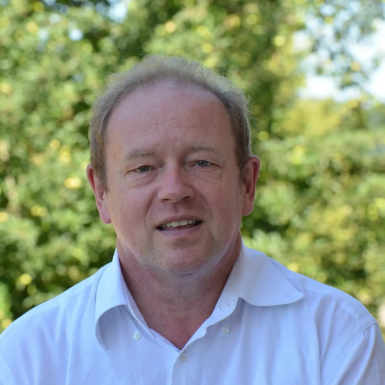 A portrait photo of Harald Floss, a white man with short blond curly hair, wearing a white button down shirt. 