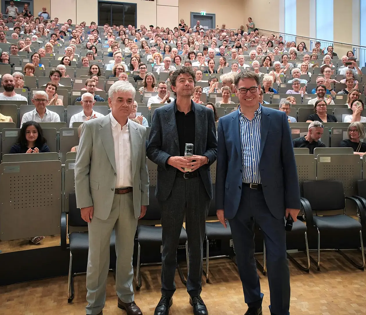 Dietmar Till, Christian Drosten, Olaf Kramer stehen vor den vollbesetzten Reihen eines Hörsaals
