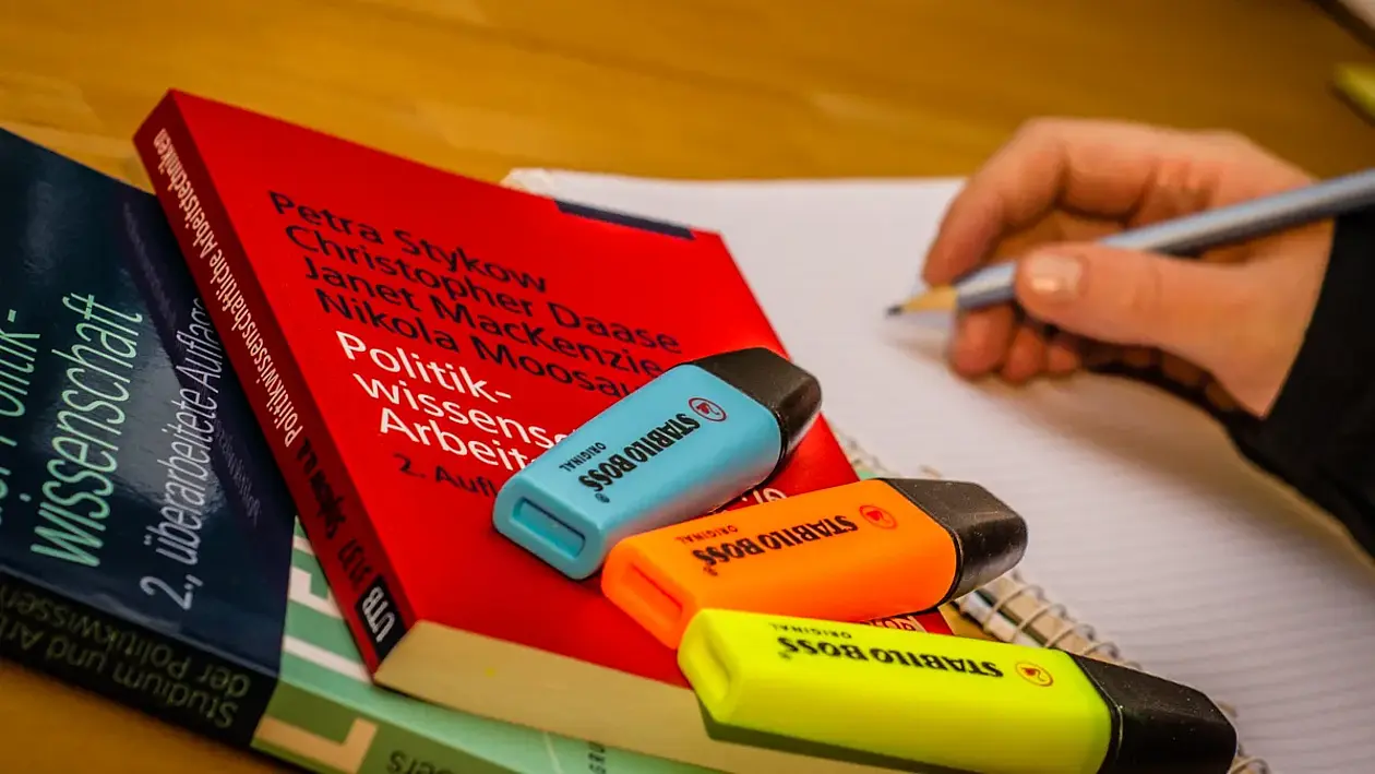 Picture showing a hand writing and books and markers.