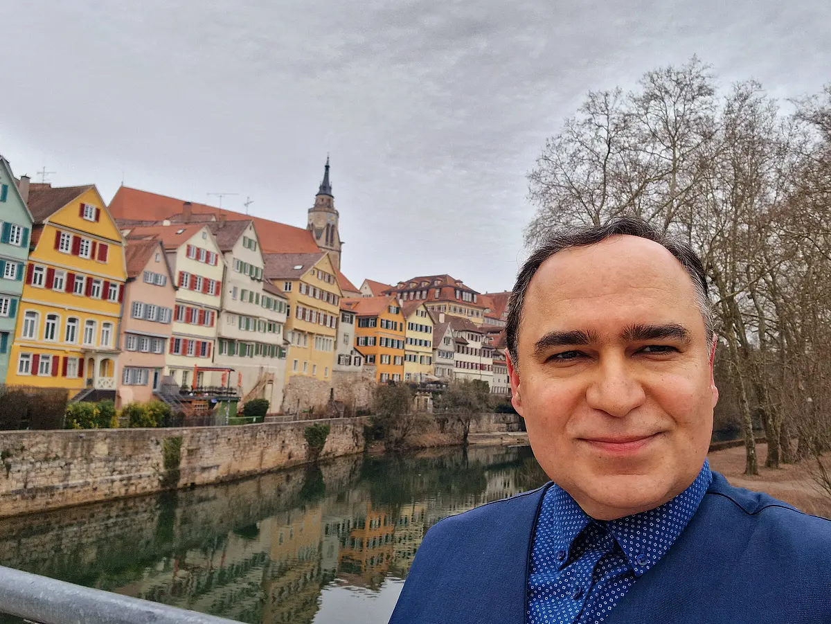 Prof. Dr. Nima Nezafati standing on Neckarbrücke in Tübingen. In the background you see houses and the church. 