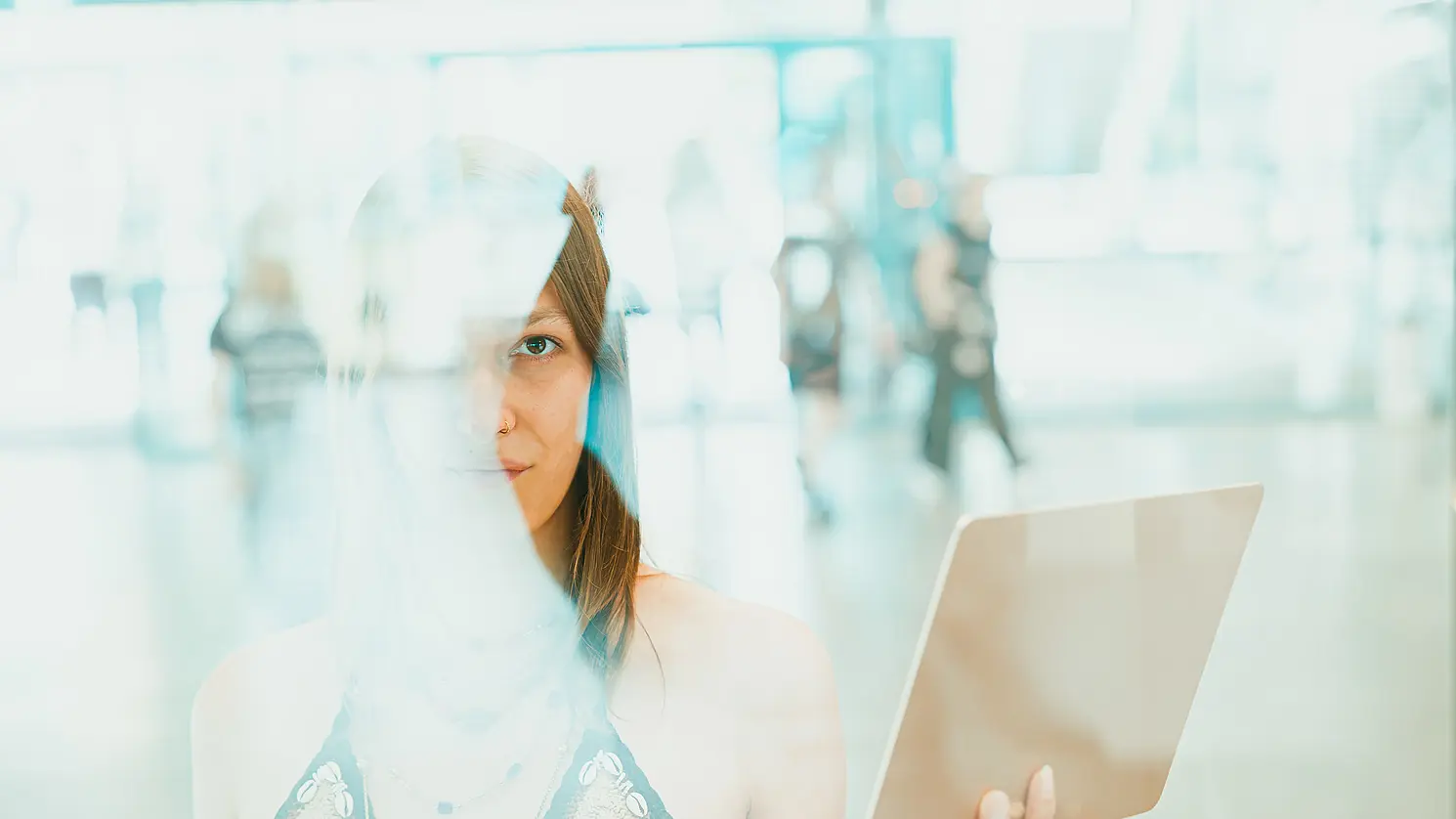 A student is standing behind a glass pane, holding a laptop