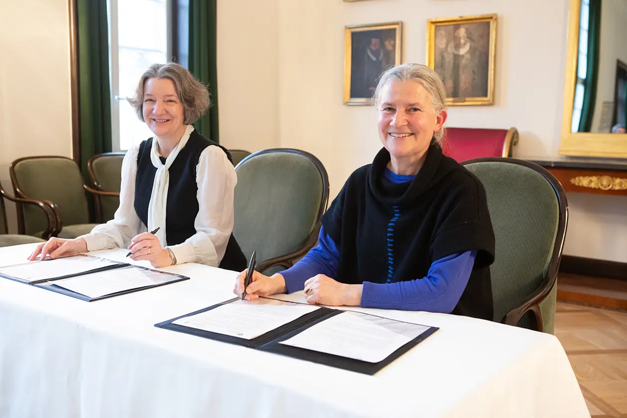 Karen O'Brien and Karla Pollmann at the table, each with a document to sign