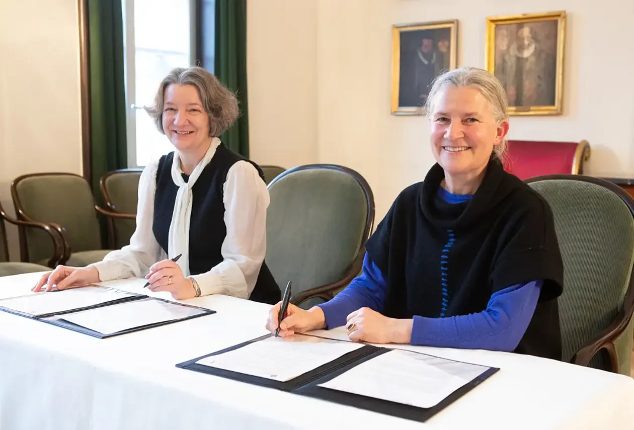 Karen O'Brien und Karla Pollmann am Tisch mit je einem Schriftstück zur Unterzeichnung