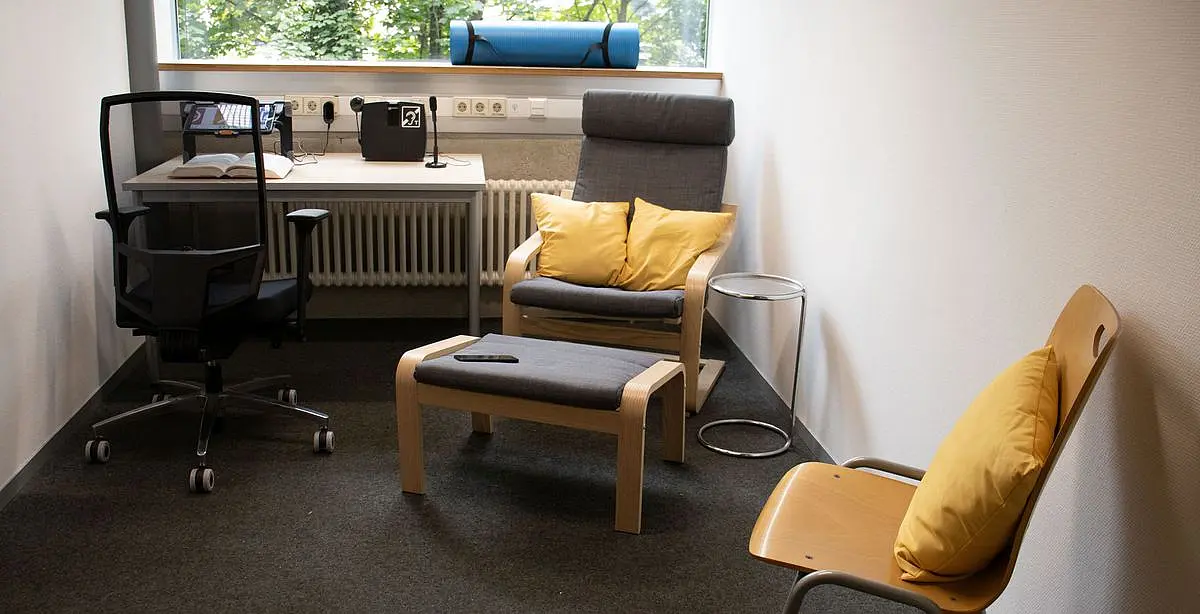 Foto des Ruhe- und Arbeitsraums A 321 in der Universitätsbibliothek, Wilhelmstraße 32. Der Raum ist barrierefrei erreichbar und mit einem höhenverstellbaren Schreibtisch, einem Sessel mit Hocker und einer Yogamatte ausgestattet.