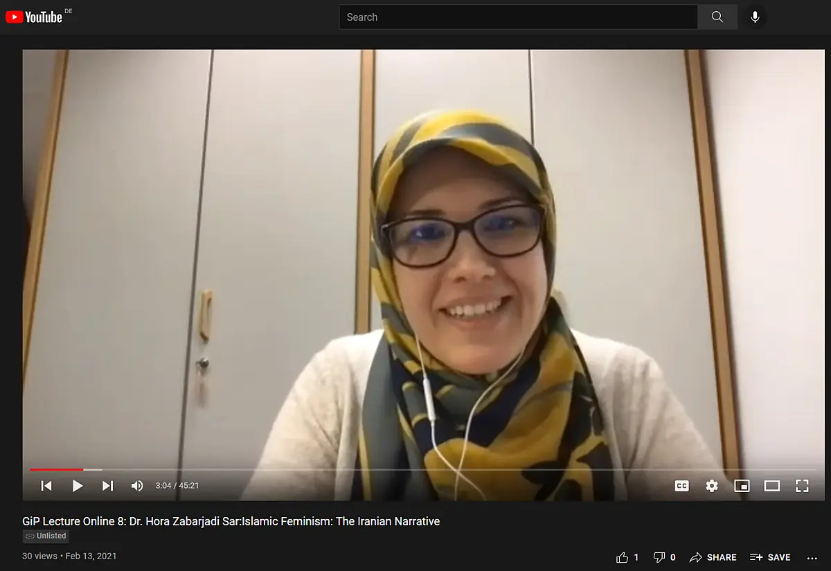 A woman with headscarf and glasses talking into a webcam