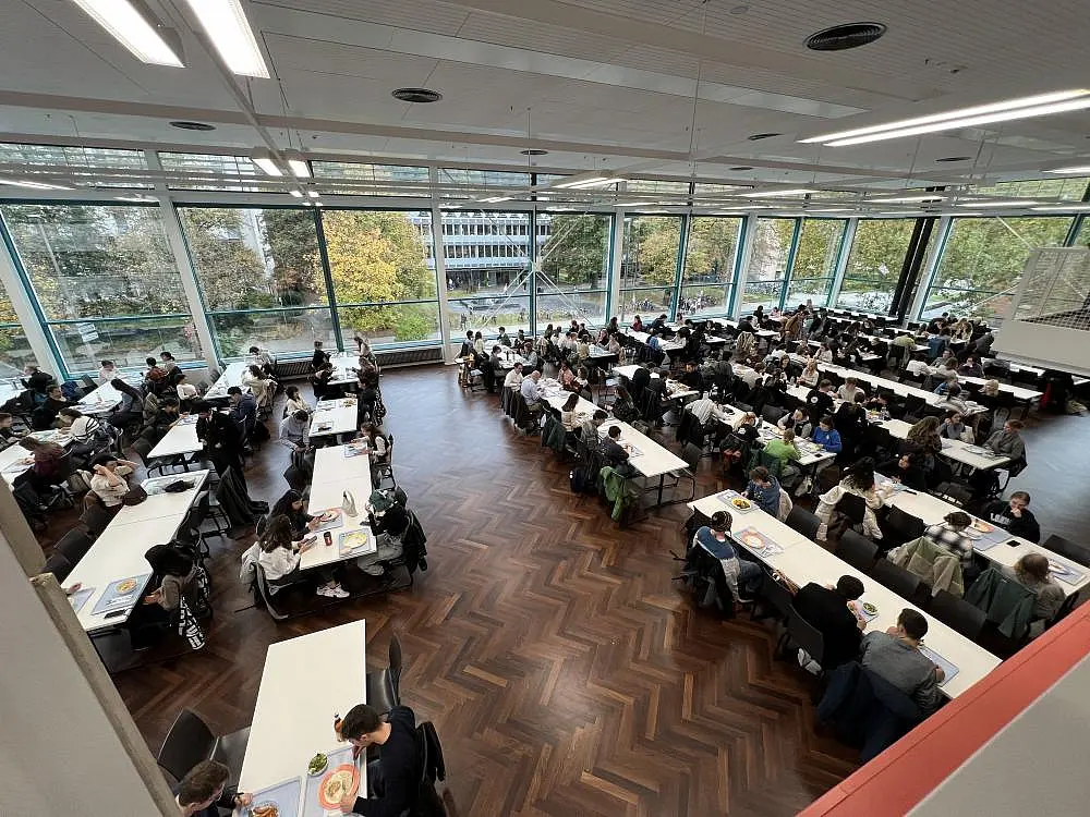 Großer Speisesaal der Mensa Wilhelmstraße von oben gesehen. Viele Studierende an den Tischen, die zu Mittag essen.