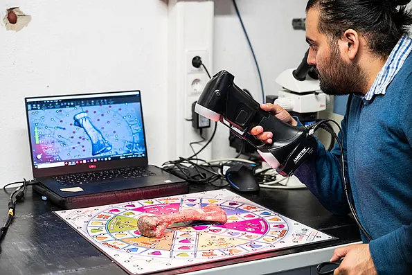 Researcher scanning a bone on a colored base with reflective points using a handheld laserschaftler erfasst einen Knochen, der auf einer farbigen Unterlage mit Punkten liegt, mit einem Handlaserscanner.