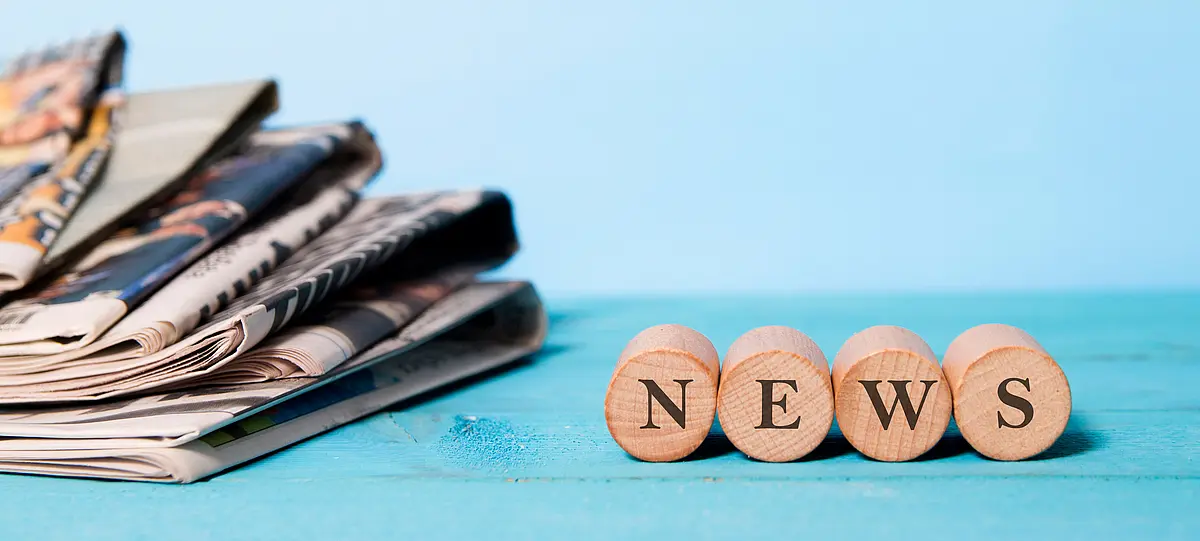 Zeitungsstapel neben Holzwürfel, auf denen "News" steht