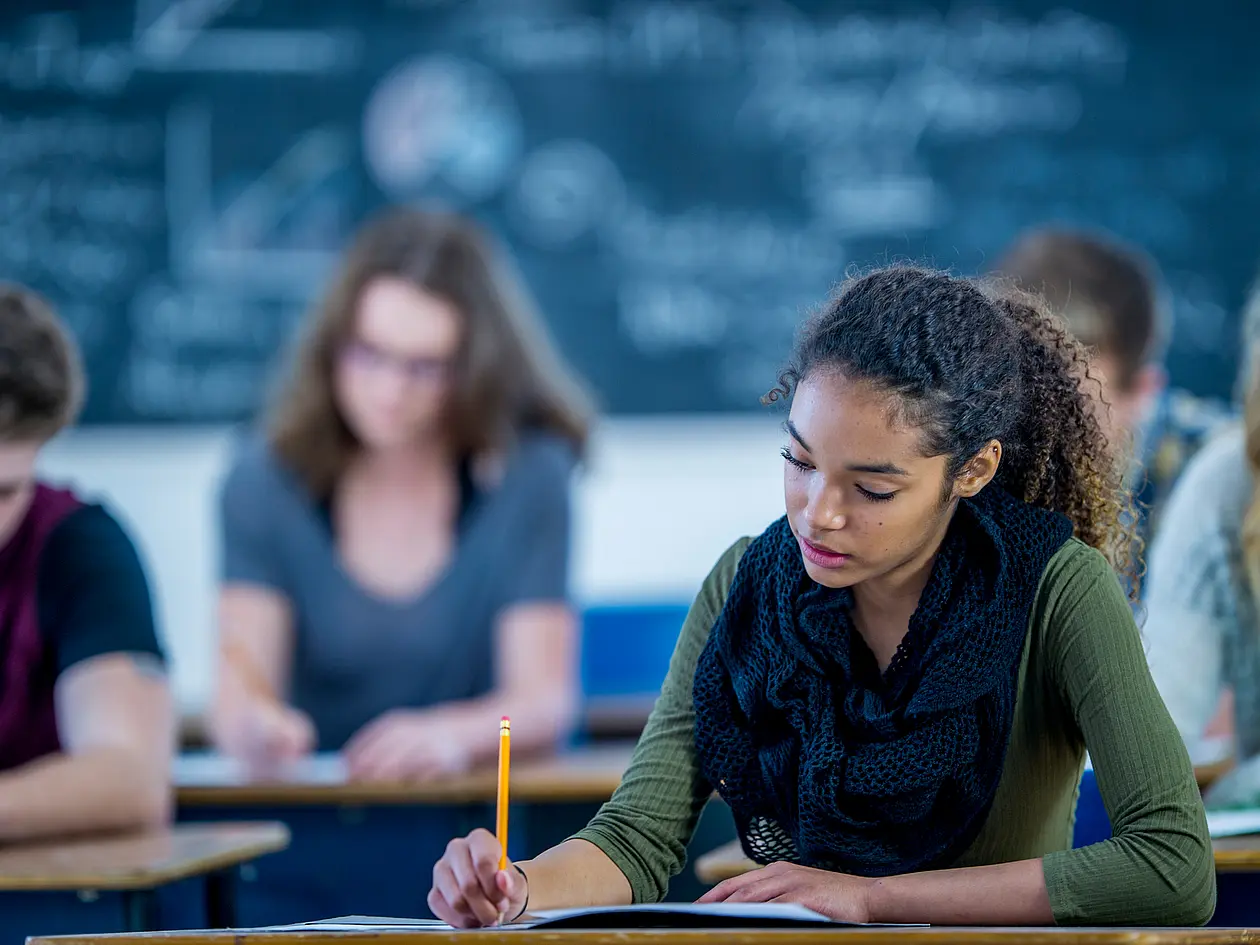Jugendliche schreiben an ihren Tischen in ihrem Klassenzimmer.